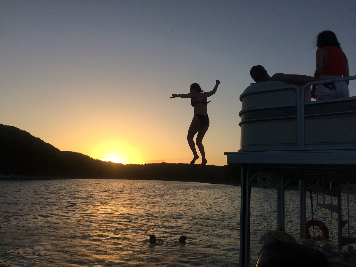 girl jumping off pontoon boat party barge on the lake